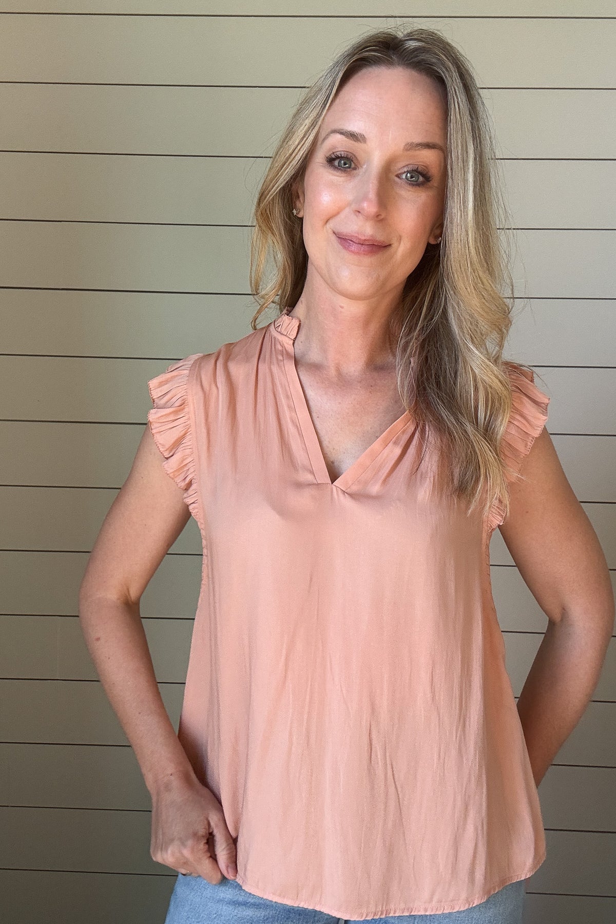 Indulge in luxurious style with our Satin Ruffle Sleeve Blouse. Crafted from lightweight satin fabric, in a warm shade of blushing peach. The v-neck and ruffled shoulders add a touch of sophistication to this sleeveless blouse. Elevate your wardrobe with this exclusive piece.
