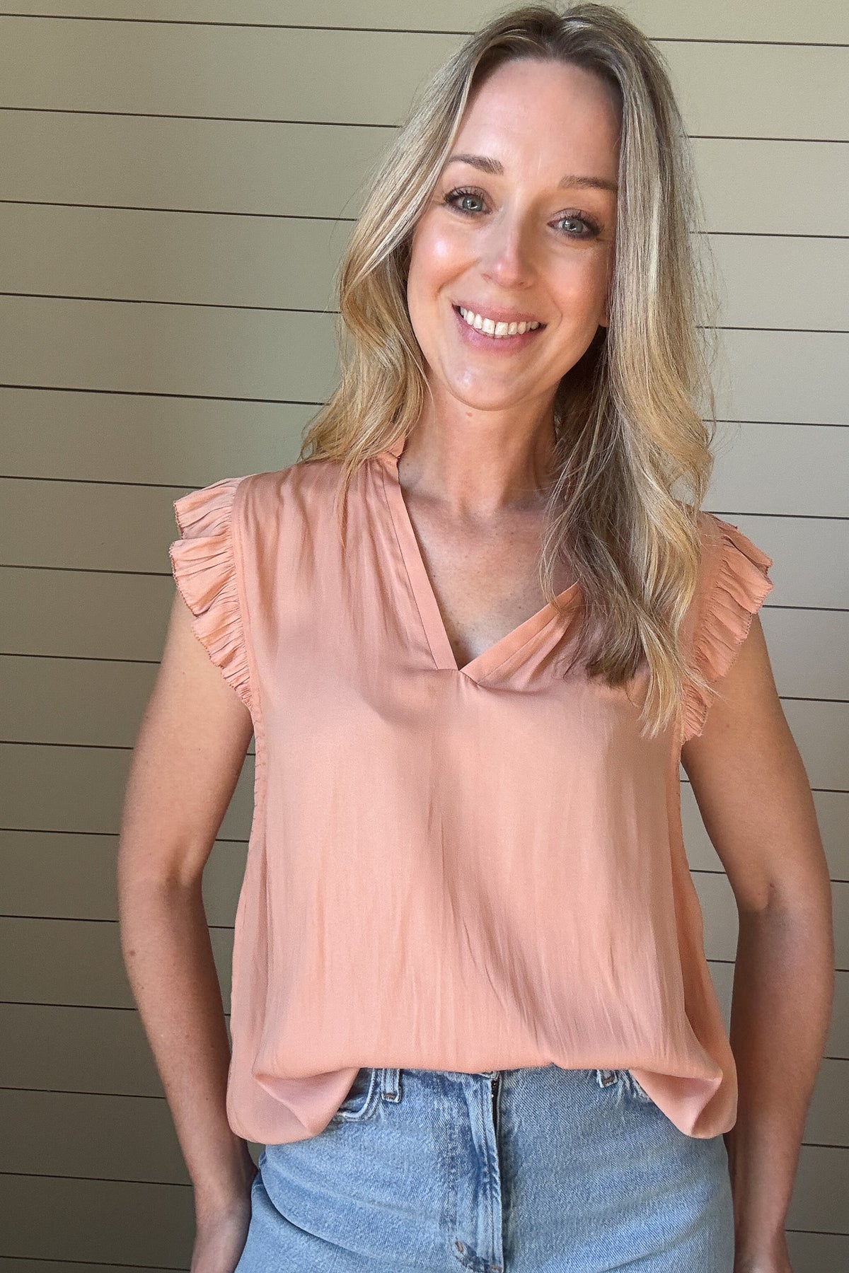 Indulge in luxurious style with our Satin Ruffle Sleeve Blouse. Crafted from lightweight satin fabric, in a warm shade of blushing peach. The v-neck and ruffled shoulders add a touch of sophistication to this sleeveless blouse. Elevate your wardrobe with this exclusive piece.