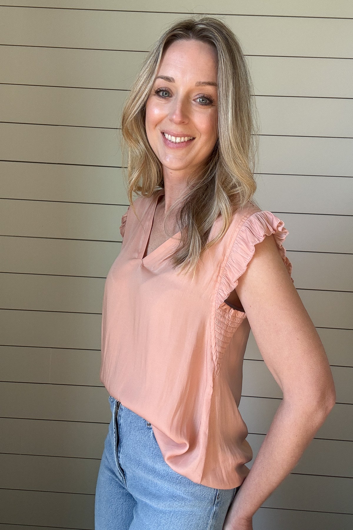 Indulge in luxurious style with our Satin Ruffle Sleeve Blouse. Crafted from lightweight satin fabric, in a warm shade of blushing peach. The v-neck and ruffled shoulders add a touch of sophistication to this sleeveless blouse. Elevate your wardrobe with this exclusive piece.