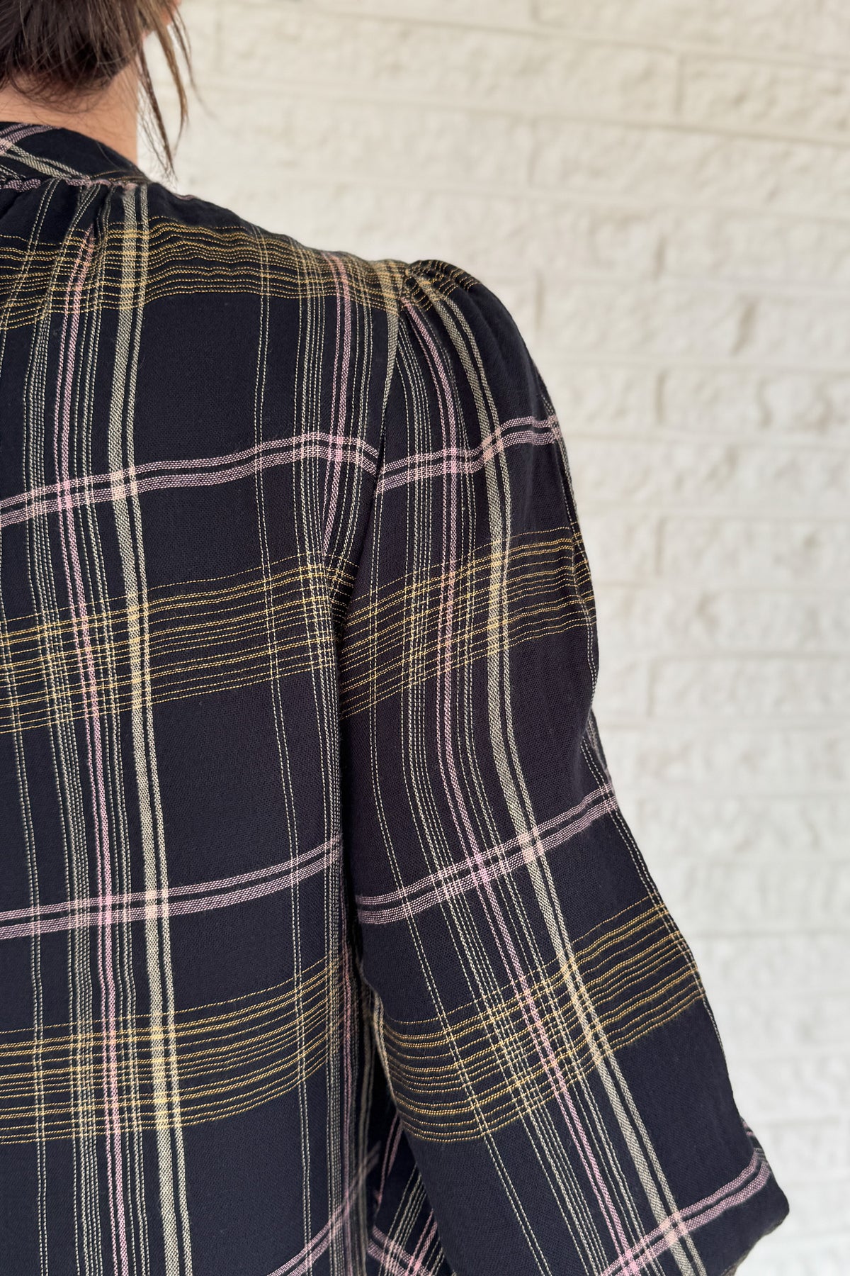  This plaid top blends classic style with feminine detail. Featuring a soft, lightweight drape, it buttons at the back of the neck for a clean finish. Smocked cuffs and subtle gathering at the neckline add texture and charm.