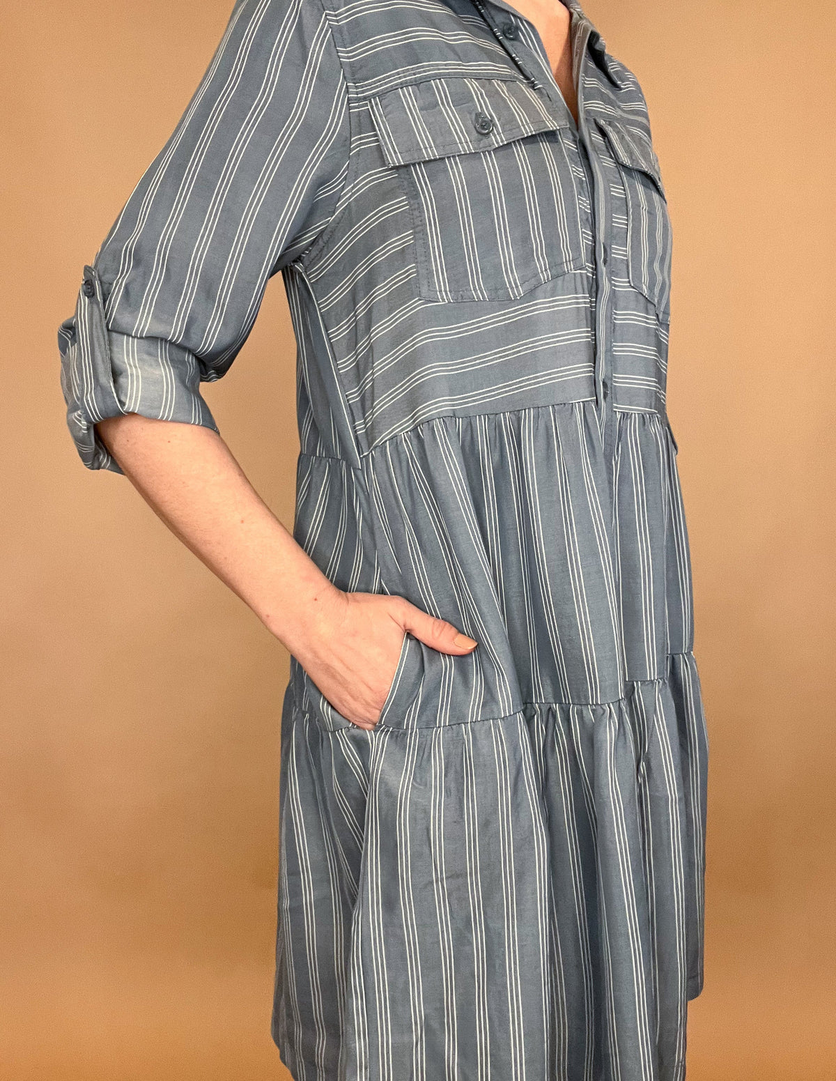 Introducing our Breezy Dress, the epitome of effortless elegance. Made from silky Tencel fabric, this button up tiered dress features a classic white pinstripe design and functional buttoned front pockets. With the ability to roll and secure the sleeves with a button tab, it's the perfect dress for any occasion. Available in blue or green.