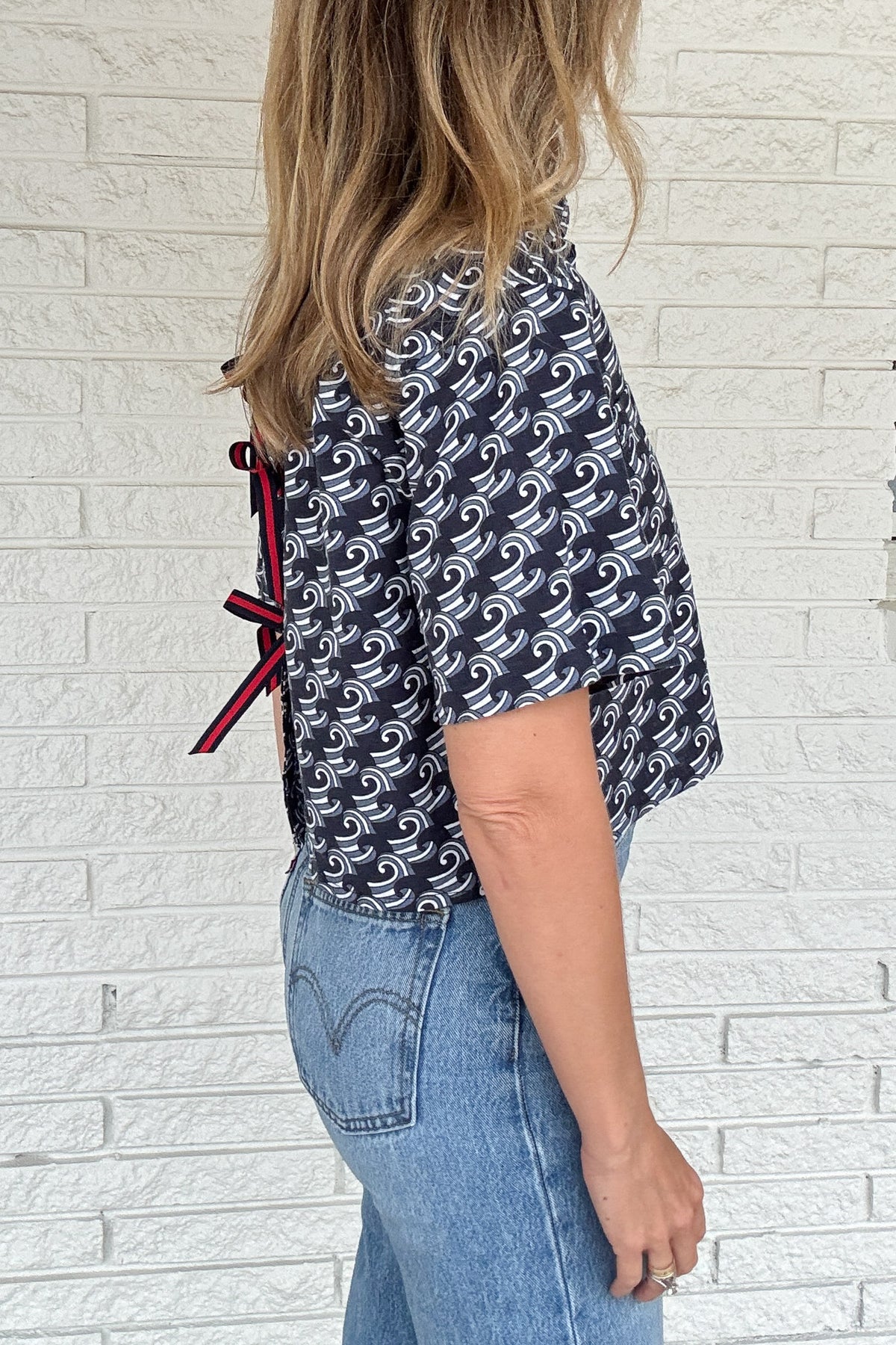 Front photo:
VonVie Harlow navy and white wave print cropped button down shirt with relaxed elbow length sleeves

Back photo:
Back view of VonVie Harlow navy wave print shirt with open back and red and navy ribbon ties