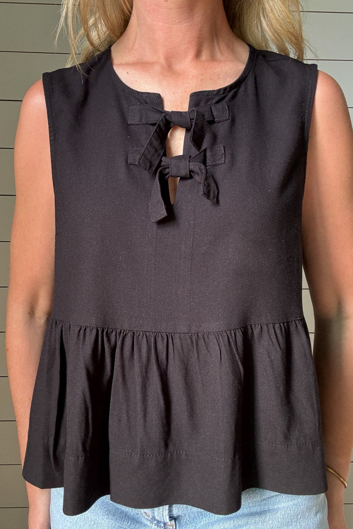 Sweet meets chic in this black top with feminine details and an easy fit. Featuring two soft bow ties at the neckline, it brings just the right touch of charm. The babydoll-style seam falls just below the ribs, giving a flattering shape without clinging. Flowy and lightweight, it moves beautifully and pairs well with denim, linen pants, or shorts. The black color keeps it classic while the silhouette adds interest and softness. An easy pick when you want something a little special without trying too hard.