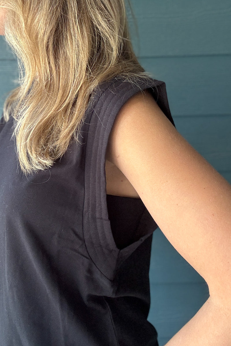 Side detail of a women’s black sleeveless top showing the structured shoulder, wide arm opening and relaxed fit.