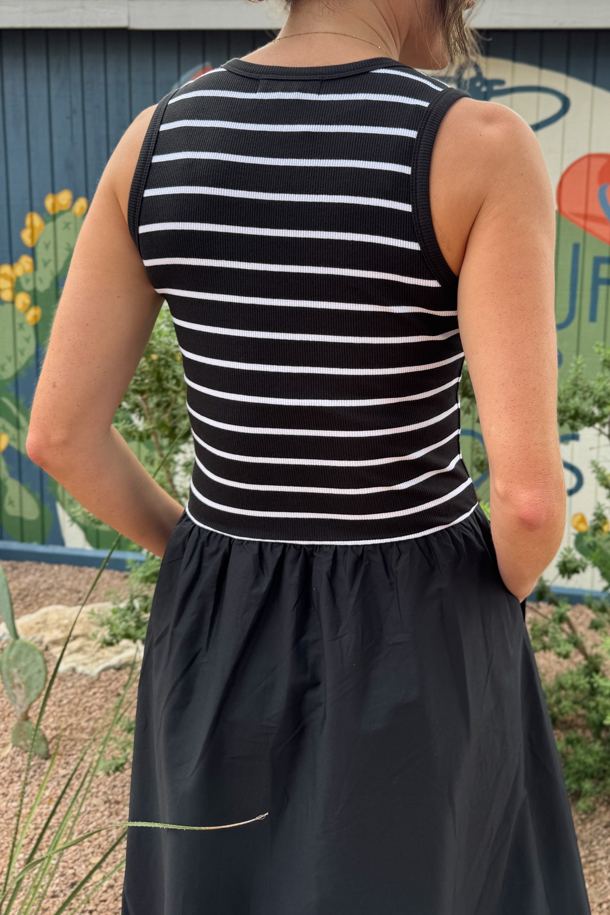 Close-up back view of a women’s black midi dress showing the fitted striped ribbed bodice and gathered waist seam.