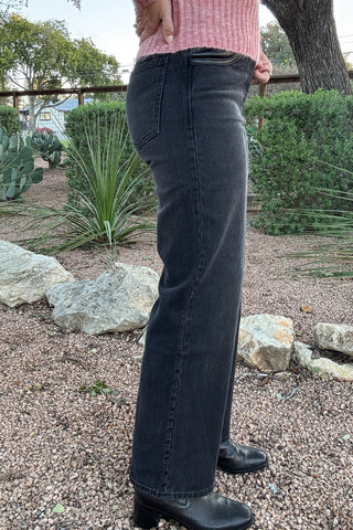 Front and back views of women's high-waisted black denim jeans with faux leather trim at the waist and pockets, a button closure, and a relaxed leg silhouette.