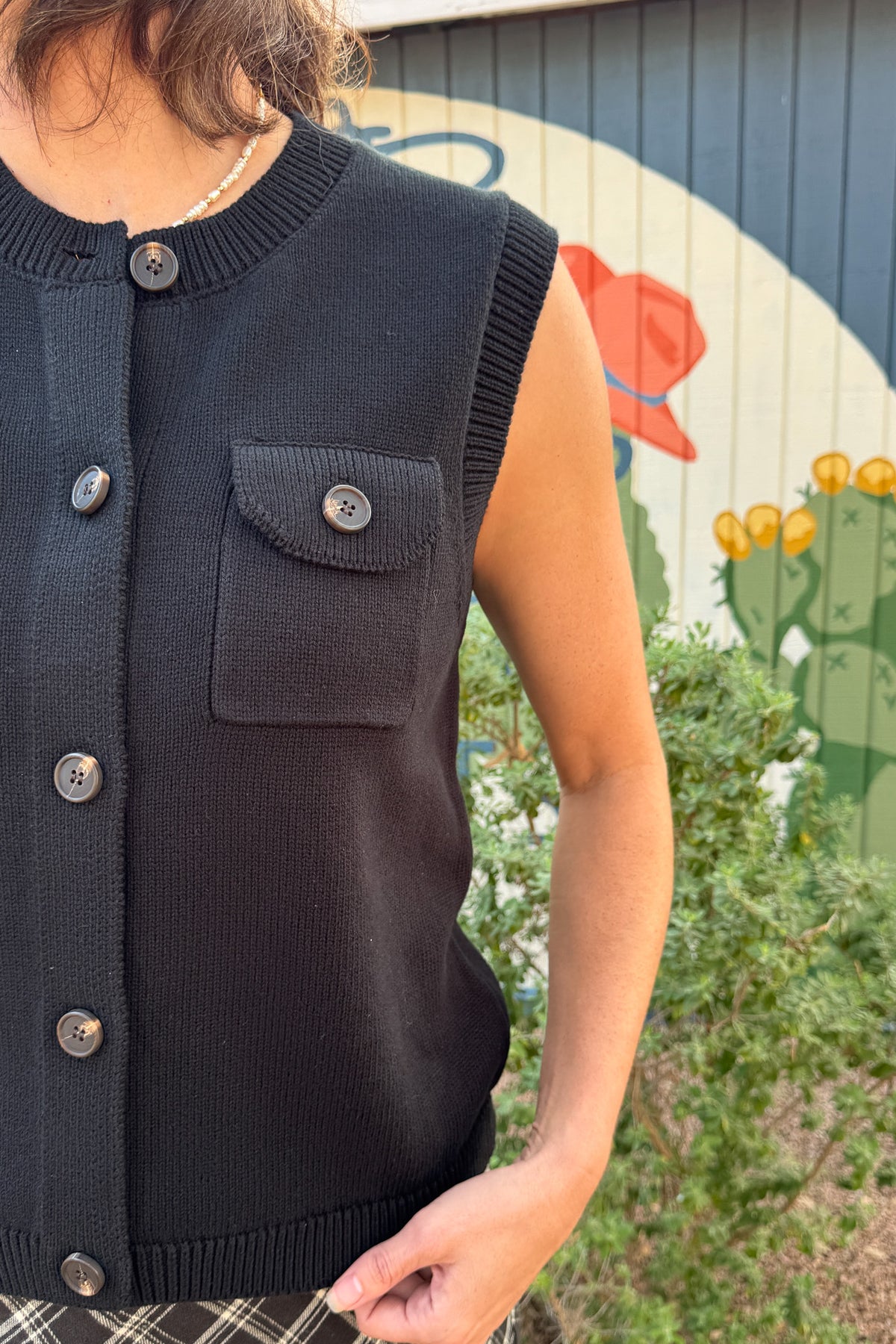 Black cotton sweater vest styled with a plaid skirt, available at Cotton & Cashmere in Blanco, Texas.
