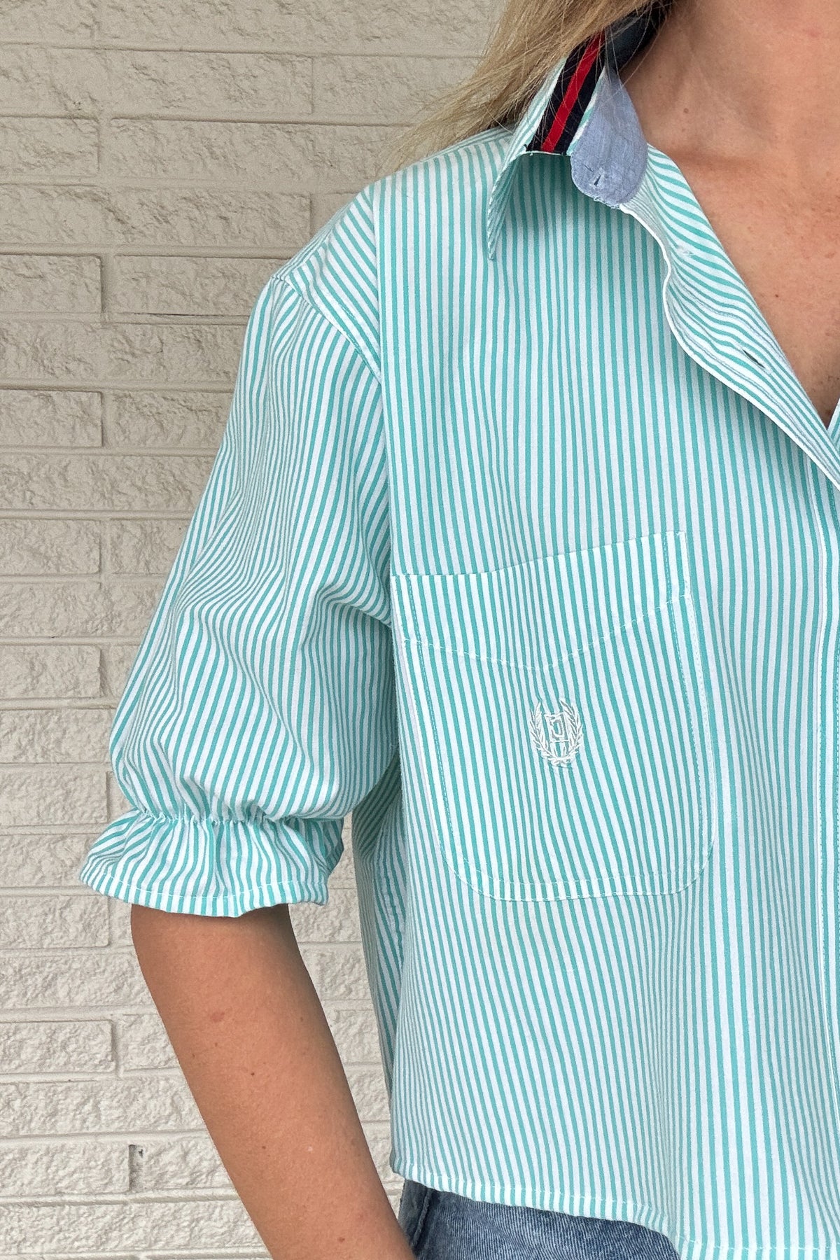 Front photo:
VonVie Harlow aqua and white striped cropped button down shirt with chest pocket, puff sleeves, and ruffled cuffs

Back photo:
Back view of VonVie Harlow aqua striped shirt with open back and red and navy ribbon ties