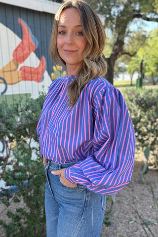 Long sleeve striped blouse for women with bold pink and blue stripes, gathered shoulder detailing, button cuffs, and a feminine tie-neck design.