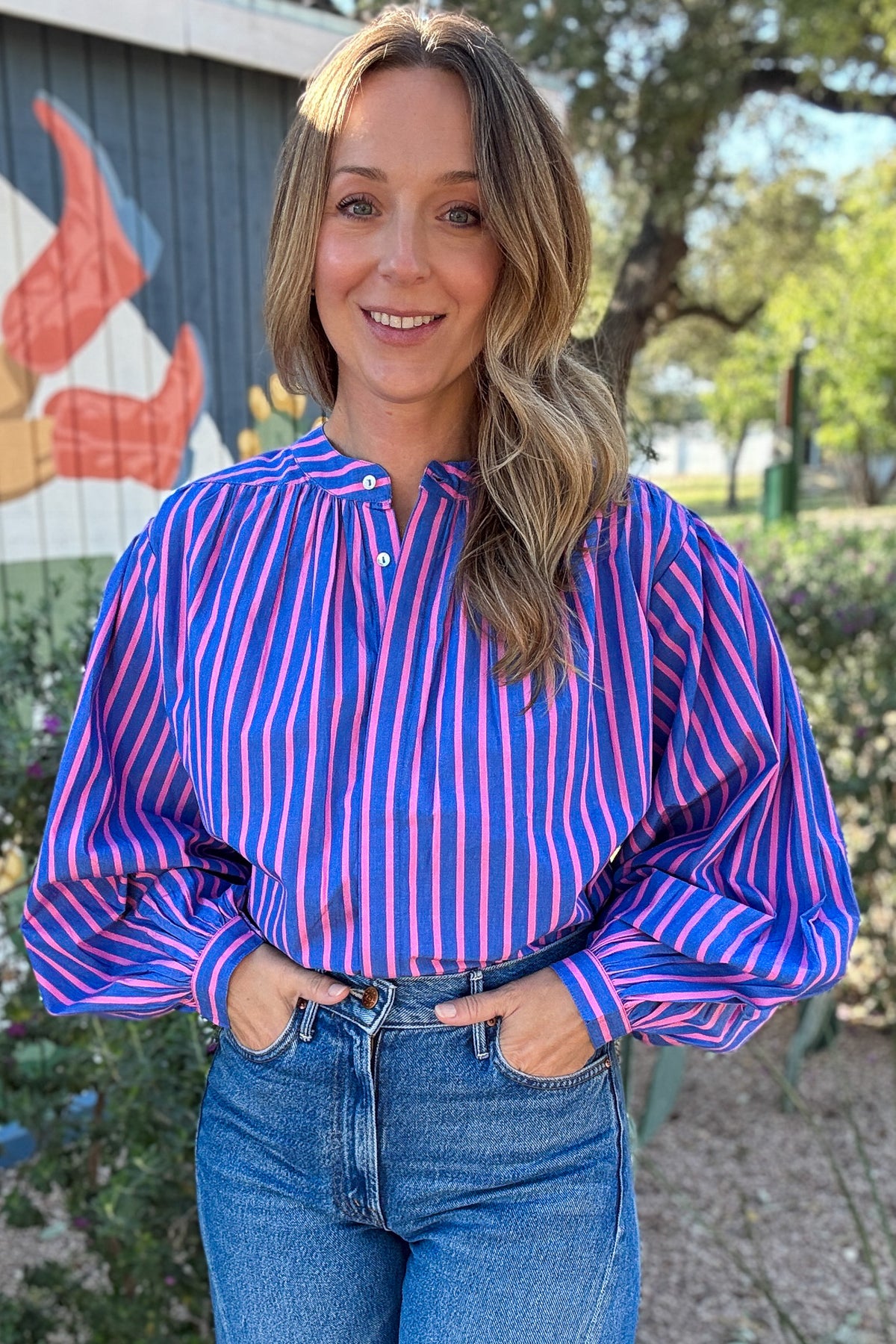 Women's pink and blue striped button-down top with a statement scarf neckline and relaxed fit, styled with high-waisted denim at Cotton & Cashmere in Blanco, Texas.