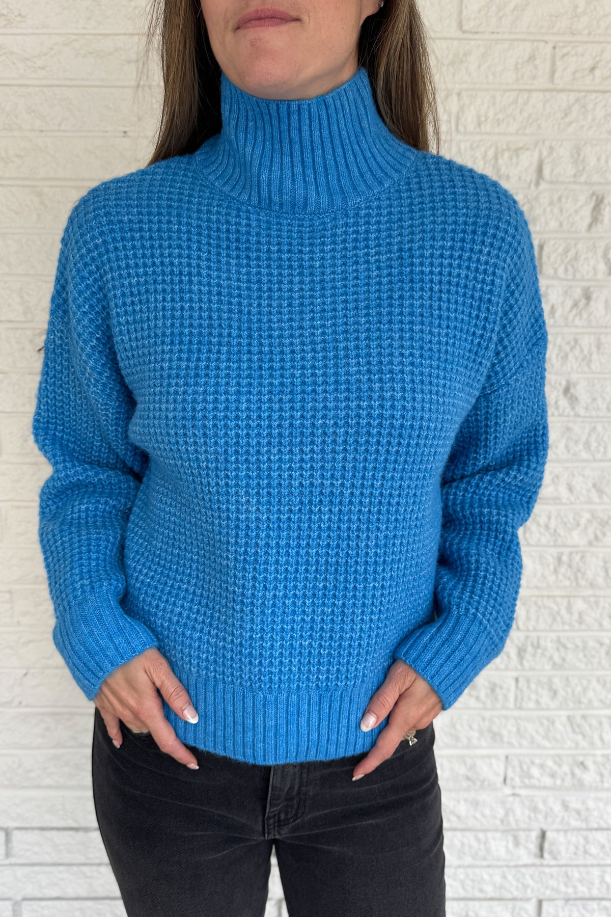 This bold blue oversized sweater brings warmth and style together in one easy piece. Knitted in a soft, textured “square” weave, it features a cozy stand-up collar and ribbed finishes that keep the look clean and structured. Perfect for pairing with denim or a skirt for effortless everyday wear.