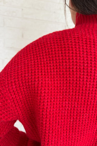 This bold red oversized sweater brings warmth and style together in one easy piece. Knitted in a soft, textured “square” weave, it features a cozy stand-up collar and ribbed finishes that keep the look clean and structured. Perfect for pairing with denim or a skirt for effortless everyday wear.
