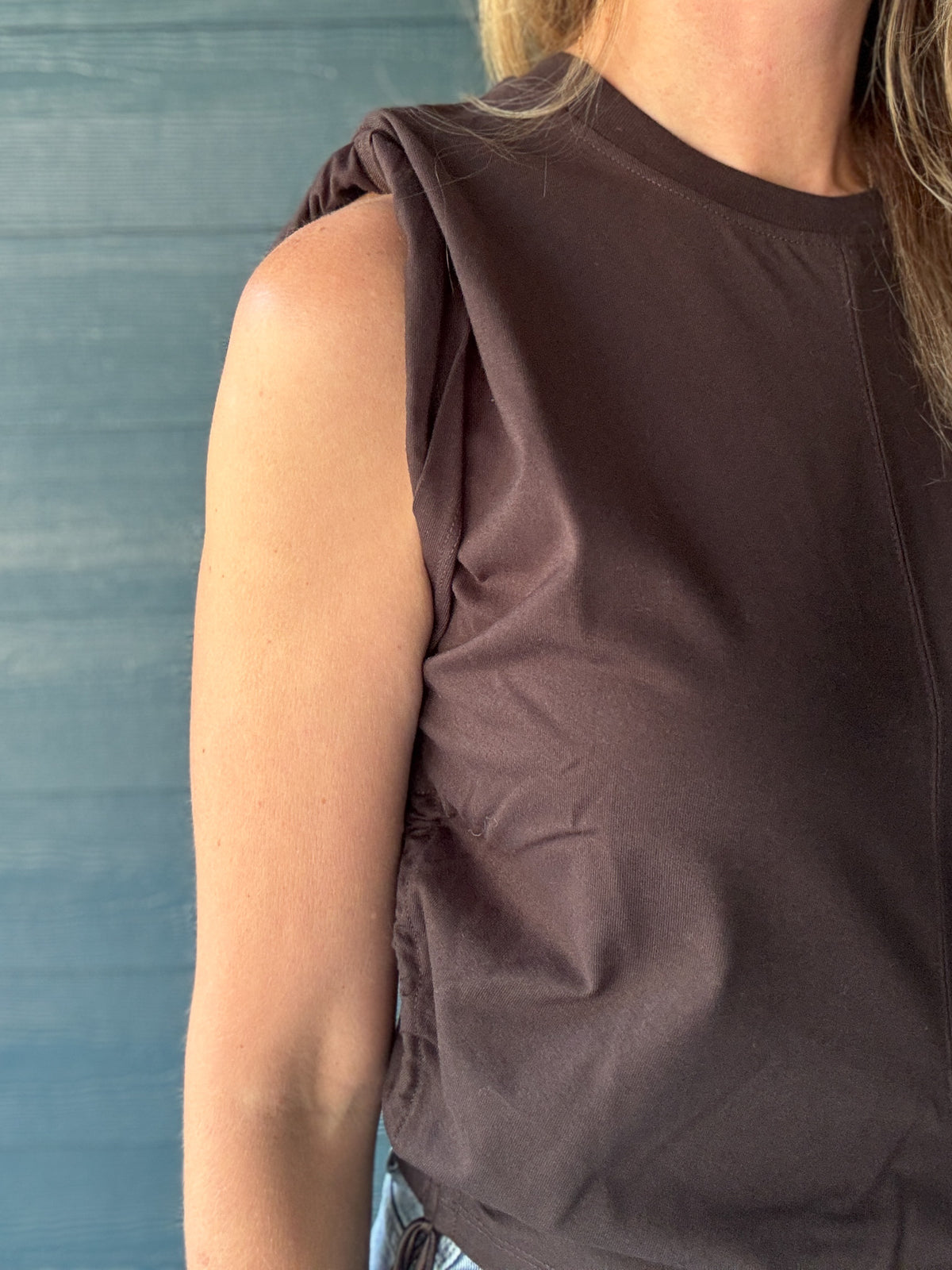 Close-up of a women’s brown sleeveless top showing the gathered shoulder detail, crew neckline and smooth knit fabric.