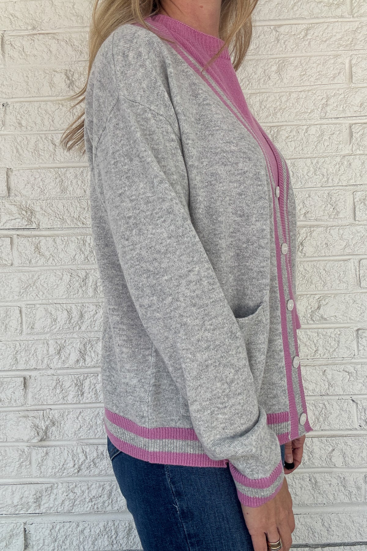 Luxury meets everyday ease in this 100% cashmere cardigan. The soft heather grey body is accented with bold pink and grey striped trim, giving a classic silhouette a modern pop of color. Lightweight yet warm, it’s the perfect piece for layering — an elevated staple for effortless clothing and everyday wear.