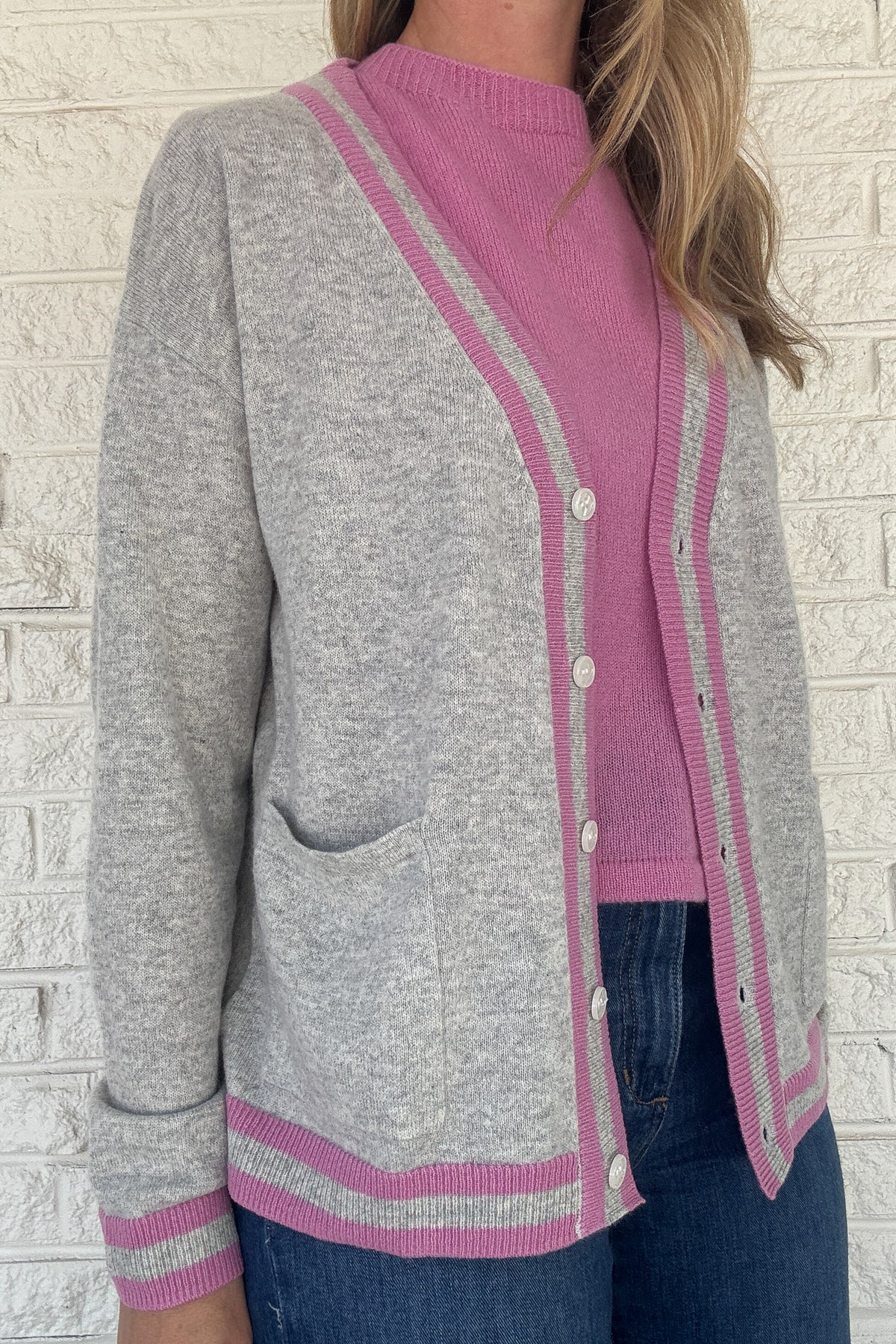 Luxury meets everyday ease in this 100% cashmere cardigan. The soft heather grey body is accented with bold pink and grey striped trim, giving a classic silhouette a modern pop of color. Lightweight yet warm, it’s the perfect piece for layering — an elevated staple for effortless clothing and everyday wear.