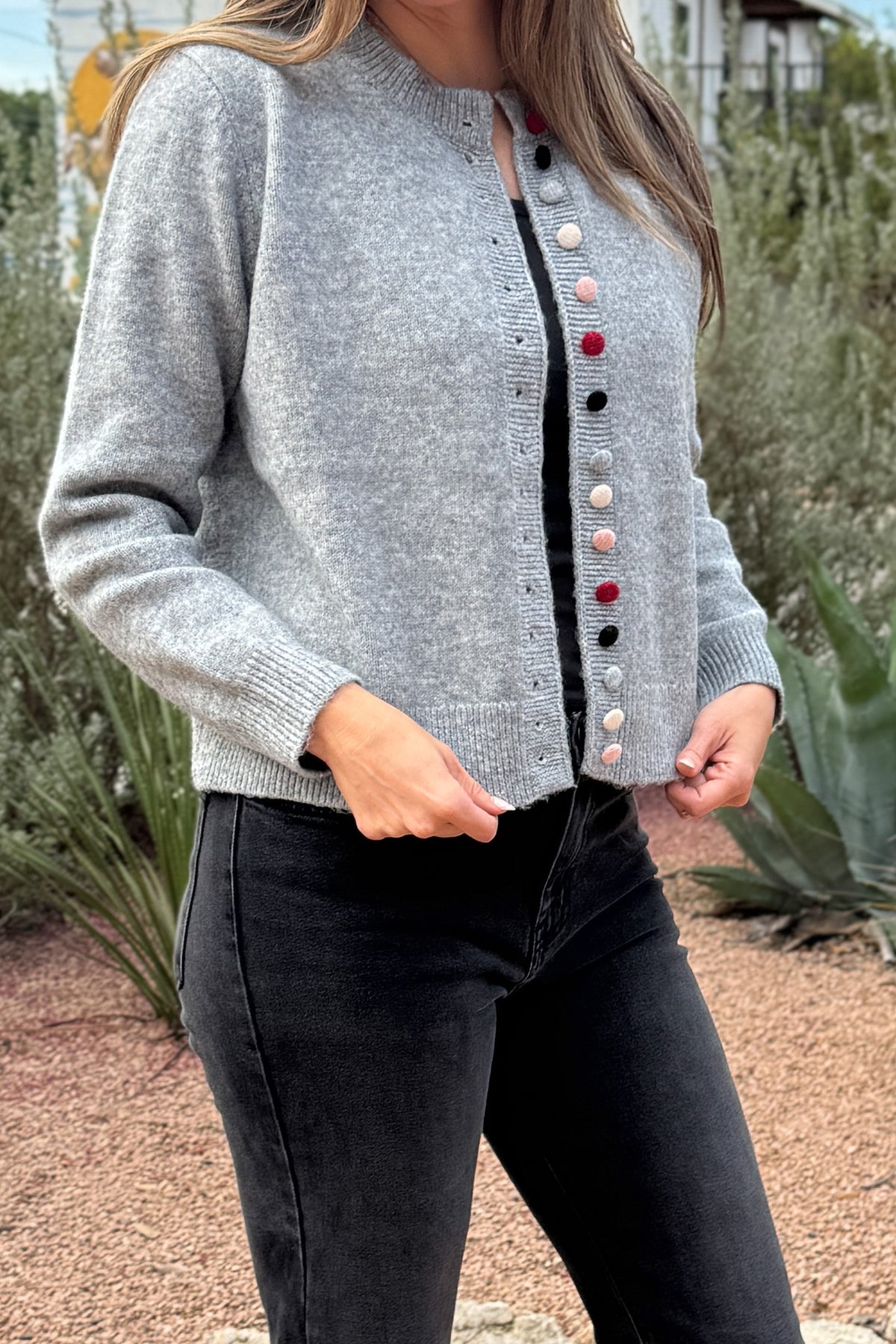 Designed in Spain, this soft grey cardigan brings a fun twist to a timeless classic. The colorful knit-covered buttons add a playful pop while keeping the look polished. It’s a cozy, easy-to-wear piece that pairs effortlessly with denim or trousers for everyday style.