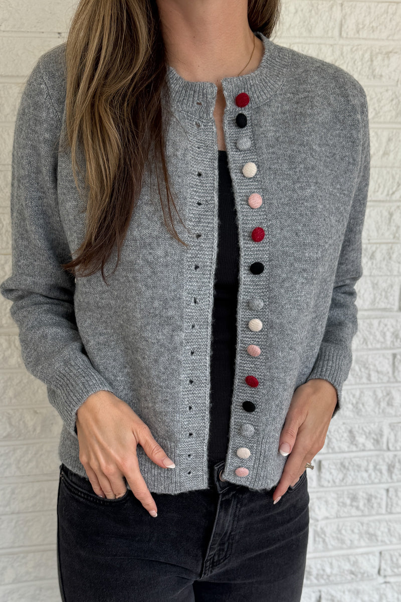 Designed in Spain, this soft grey cardigan brings a fun twist to a timeless classic. The colorful knit-covered buttons add a playful pop while keeping the look polished. It’s a cozy, easy-to-wear piece that pairs effortlessly with denim or trousers for everyday style.