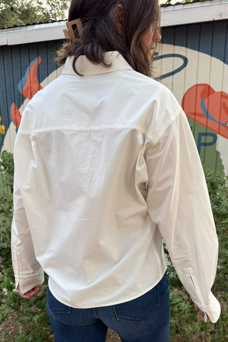 Relaxed white cotton shirt for women featuring a utility-style pocket, dropped shoulders, and slightly cropped length.
