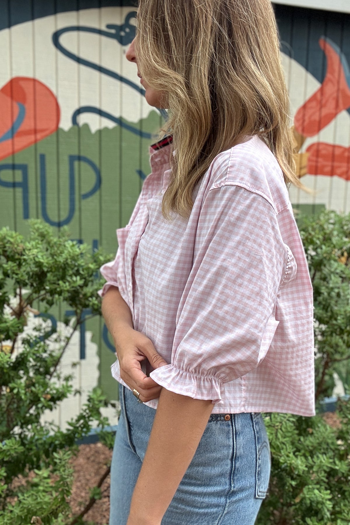 Back photo:
Back view of VonVie Harlow pink gingham cropped shirt with open back and red and navy ribbon ties

Side photo:
Side view of VonVie Harlow pink gingham shirt with puff sleeves, ruffled cuffs, and a relaxed cropped fit