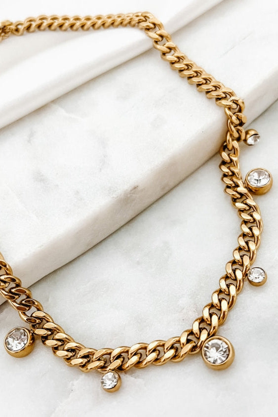 Gold chain necklace with crystal pendants on a marble surface