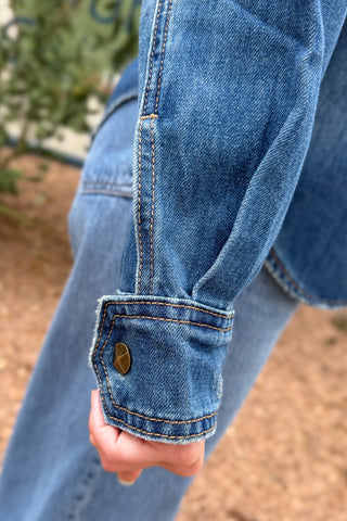 cuff details women’s studded denim shirt jacket in medium wash with antique gold stud details, western-inspired seams and front patch pockets at Cotton & Cashmere in Blanco, Texas.
