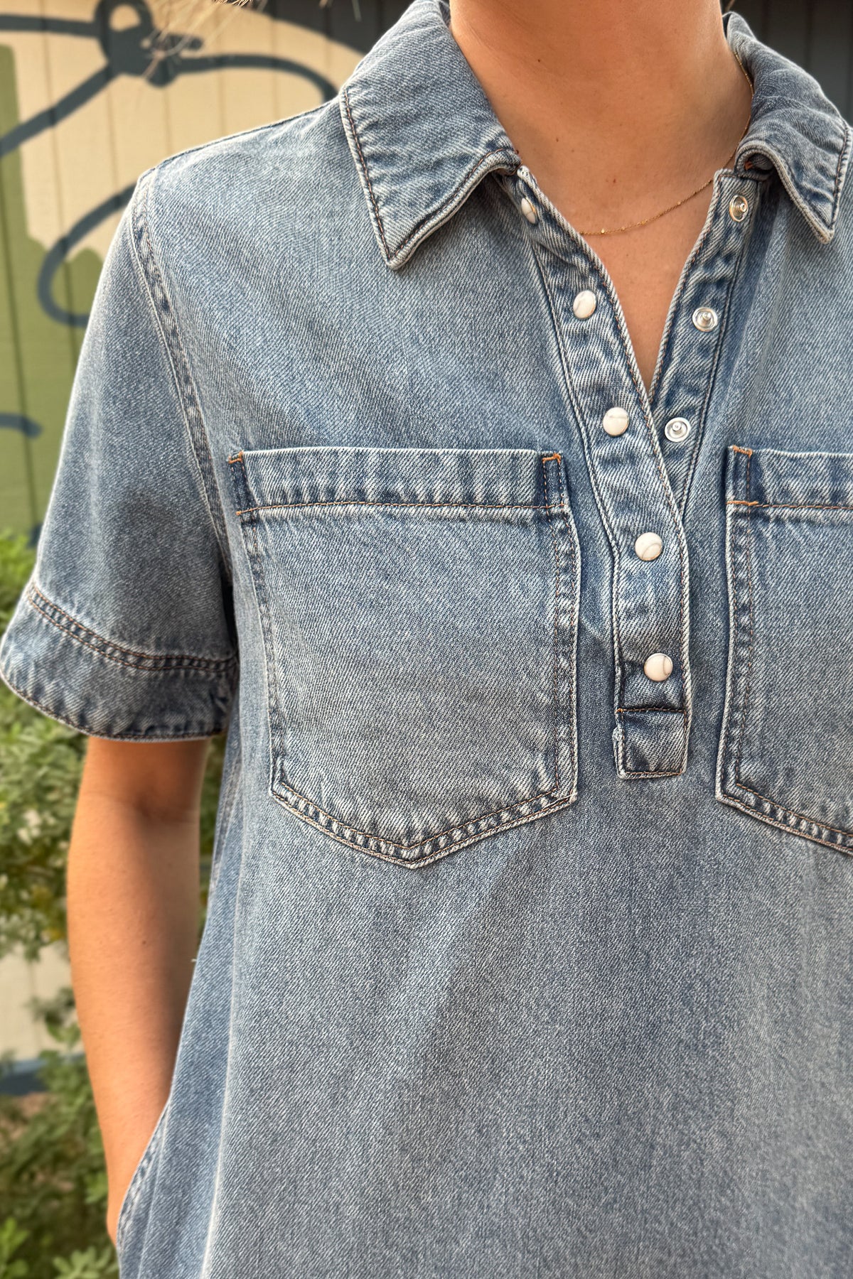 Close-up of a women’s denim shirt dress featuring a pointed collar, pearl snap placket and two oversized chest pockets.