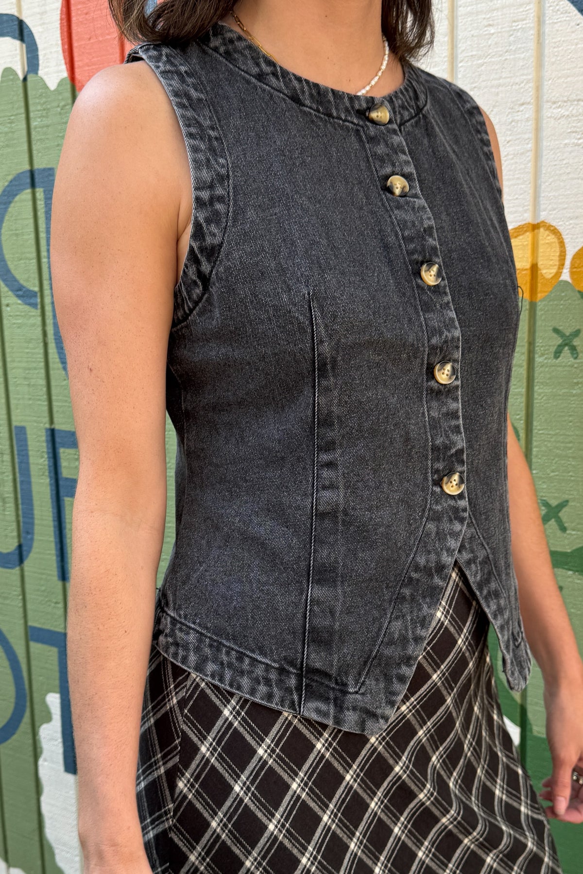 Women’s washed black 100% cotton denim vest with asymmetrical button front and fitted seamed silhouette.