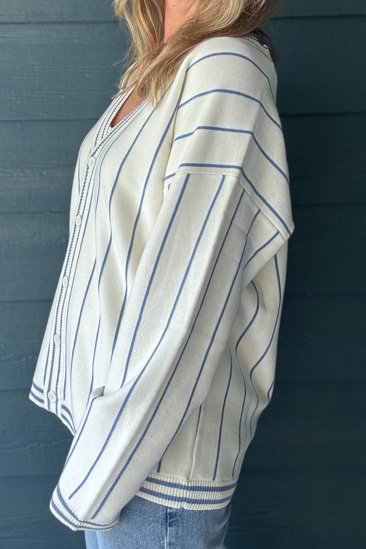 Side view of FRNCH ivory and blue striped cardigan sweater showing dropped shoulders, relaxed fit and long sleeves.