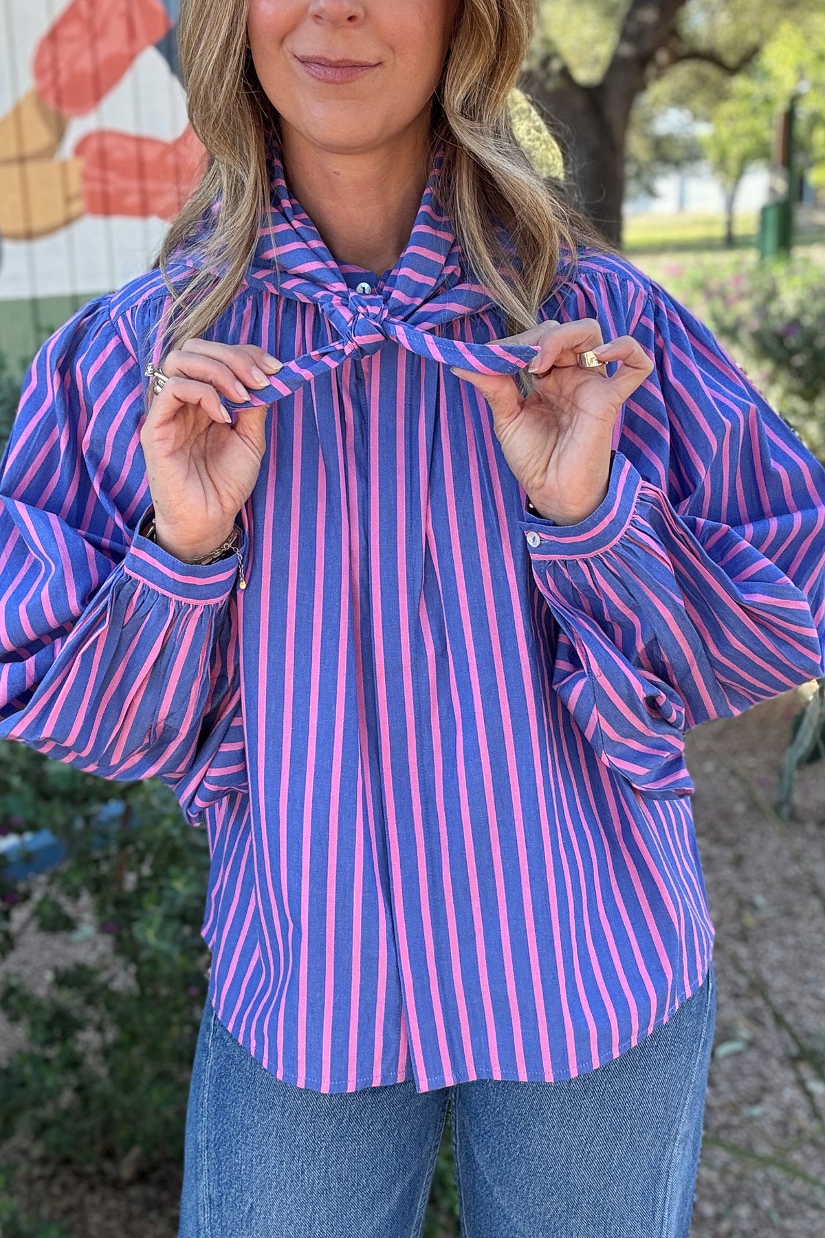 Statement striped blouse for women featuring vibrant pink and blue vertical stripes, a button-front neckline, and oversized balloon sleeves. Available at Cotton & Cashmere Boutique.