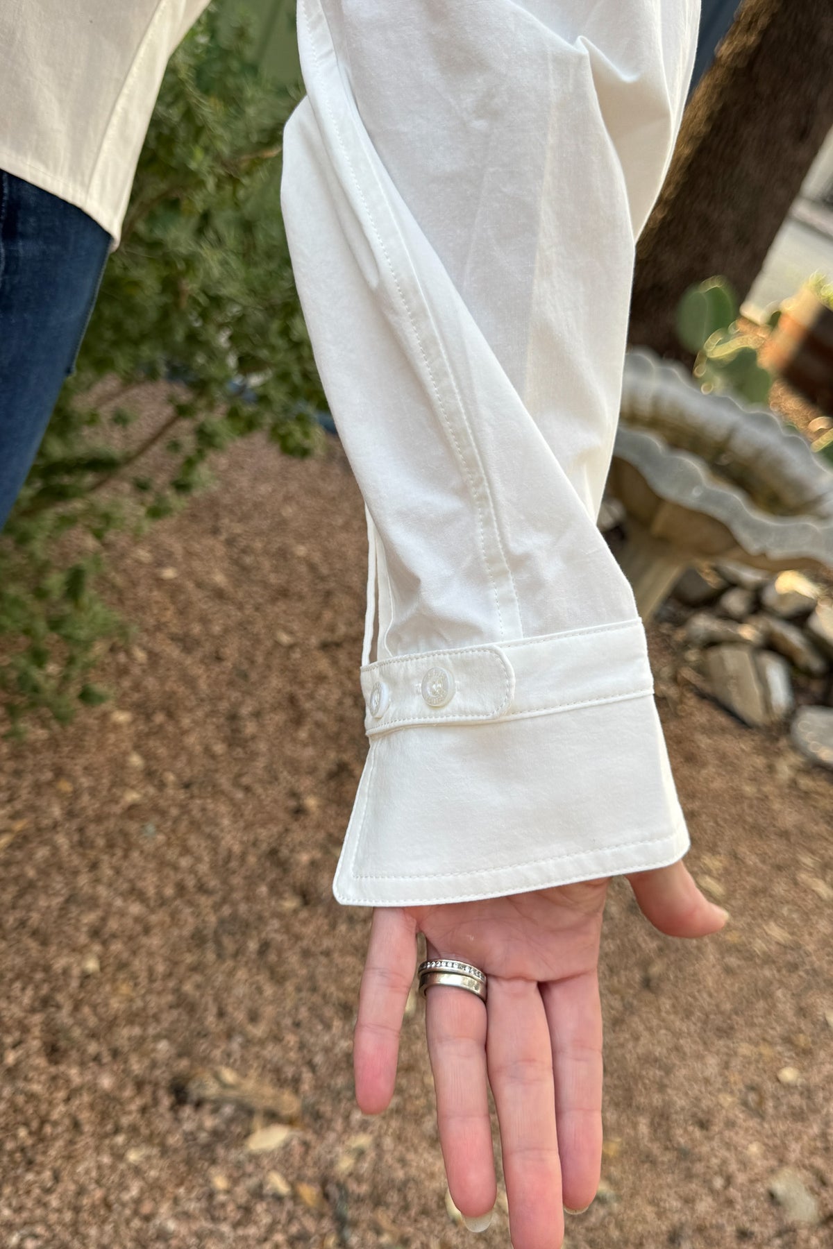 Close-up of wide button cuff detail on a women’s white cotton utility shirt, available at Cotton & Cashmere in Blanco, Texas.