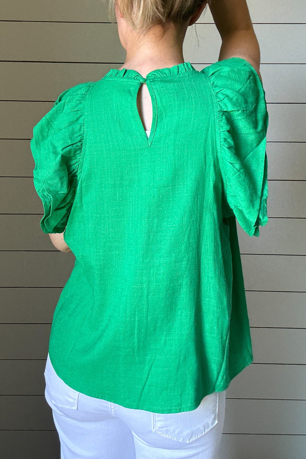 Say hello to your new favorite top. This bright green blouse by THML is all about effortless style with standout details. Made from a woven fabric, it features delicate pleating and smocking across the chest for texture and charm. The flutter sleeves add a soft, feminine touch while keeping it breezy and cool. A high neckline keeps it polished, making it perfect for work or weekend wear. Style it with white denim or tuck it into a skirt, easy either way. It’s a vibrant pop of color for your spring-to-summer