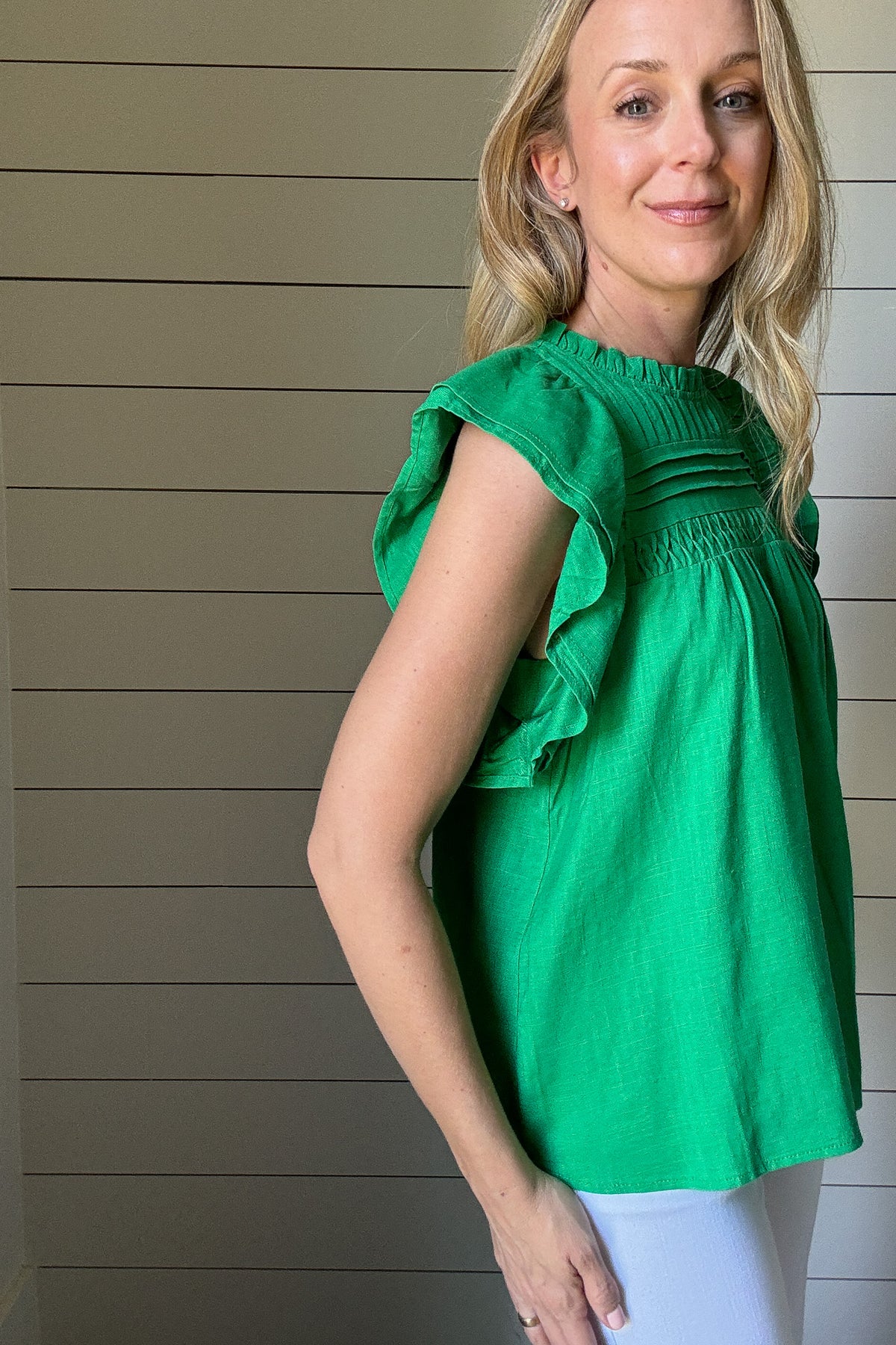 Say hello to your new favorite top. This bright green blouse by THML is all about effortless style with standout details. Made from a woven fabric, it features delicate pleating and smocking across the chest for texture and charm. The flutter sleeves add a soft, feminine touch while keeping it breezy and cool. A high neckline keeps it polished, making it perfect for work or weekend wear. Style it with white denim or tuck it into a skirt, easy either way. It’s a vibrant pop of color for your spring-to-summer