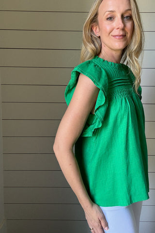 Say hello to your new favorite top. This bright green blouse by THML is all about effortless style with standout details. Made from a woven fabric, it features delicate pleating and smocking across the chest for texture and charm. The flutter sleeves add a soft, feminine touch while keeping it breezy and cool. A high neckline keeps it polished, making it perfect for work or weekend wear. Style it with white denim or tuck it into a skirt, easy either way. It’s a vibrant pop of color for your spring-to-summer