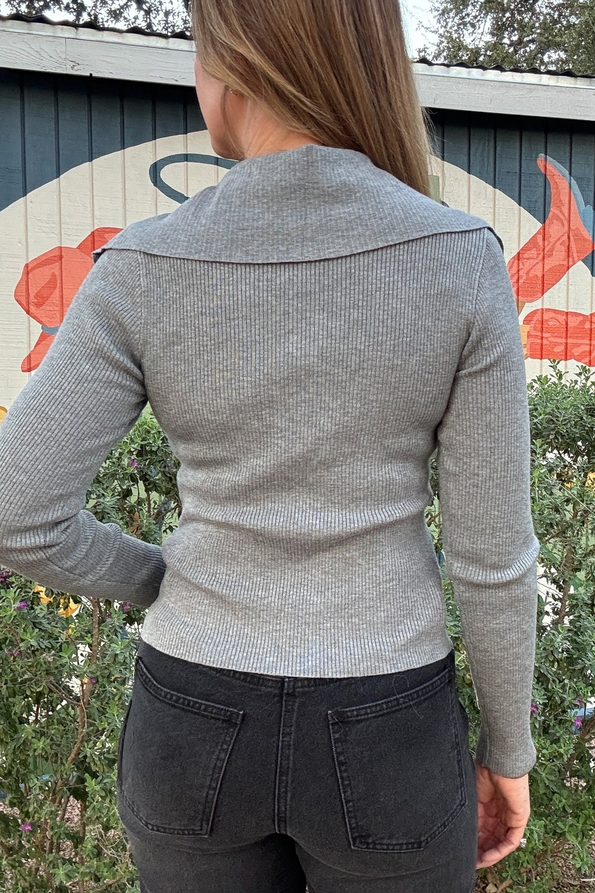 Women's gray button-front knit top with delicate ruffles, a wide collar, and a flattering fitted silhouette. Styled with black denim at Cotton & Cashmere in Blanco, Texas.