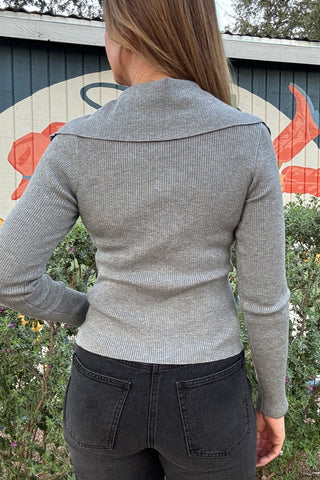 Women's gray button-front knit top with delicate ruffles, a wide collar, and a flattering fitted silhouette. Styled with black denim at Cotton & Cashmere in Blanco, Texas.