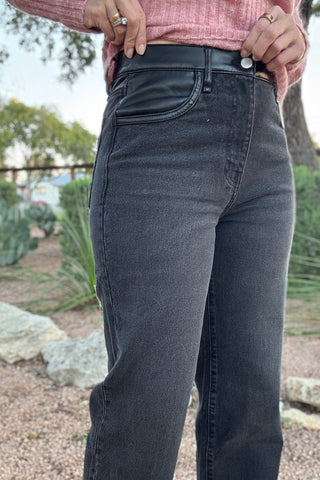 High-rise washed black denim jeans for women with a smooth black faux leather waistband, belt loops, and classic five-pocket styling.