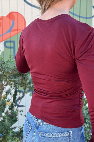 Wine red long sleeve top for women with gathered side seams, soft draping across the front, and a feminine fitted design
