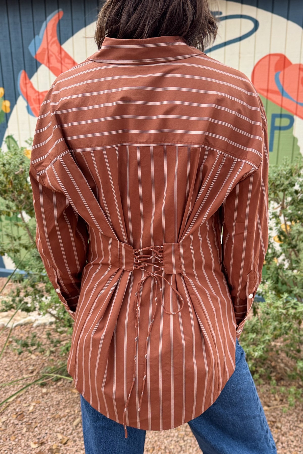 A rust striped button down top with an easy, relaxed fit and a unique lace up back detail. This women’s collared shirt features long sleeves, button cuffs, and an adjustable back that lets you create more shape at the waist. An effortless top to pair with jeans, trousers, or skirts for everyday wear.