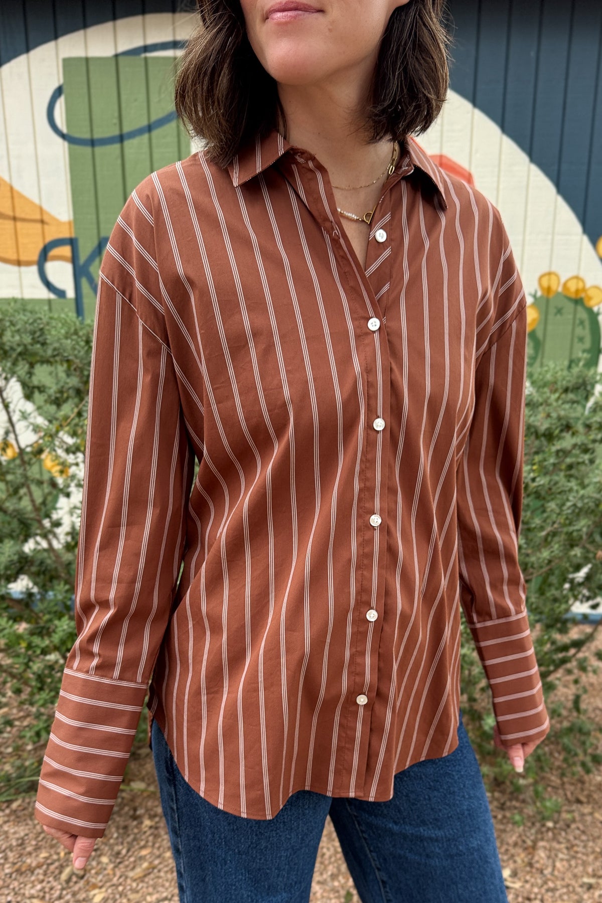 A rust striped button down top with an easy, relaxed fit and a unique lace up back detail. This women’s collared shirt features long sleeves, button cuffs, and an adjustable back that lets you create more shape at the waist. An effortless top to pair with jeans, trousers, or skirts for everyday wear.