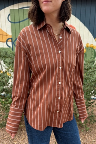 A rust striped button down top with an easy, relaxed fit and a unique lace up back detail. This women’s collared shirt features long sleeves, button cuffs, and an adjustable back that lets you create more shape at the waist. An effortless top to pair with jeans, trousers, or skirts for everyday wear.