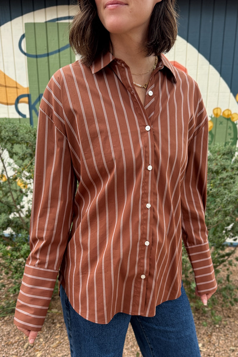 A rust striped button down top with an easy, relaxed fit and a unique lace up back detail. This women’s collared shirt features long sleeves, button cuffs, and an adjustable back that lets you create more shape at the waist. An effortless top to pair with jeans, trousers, or skirts for everyday wear.