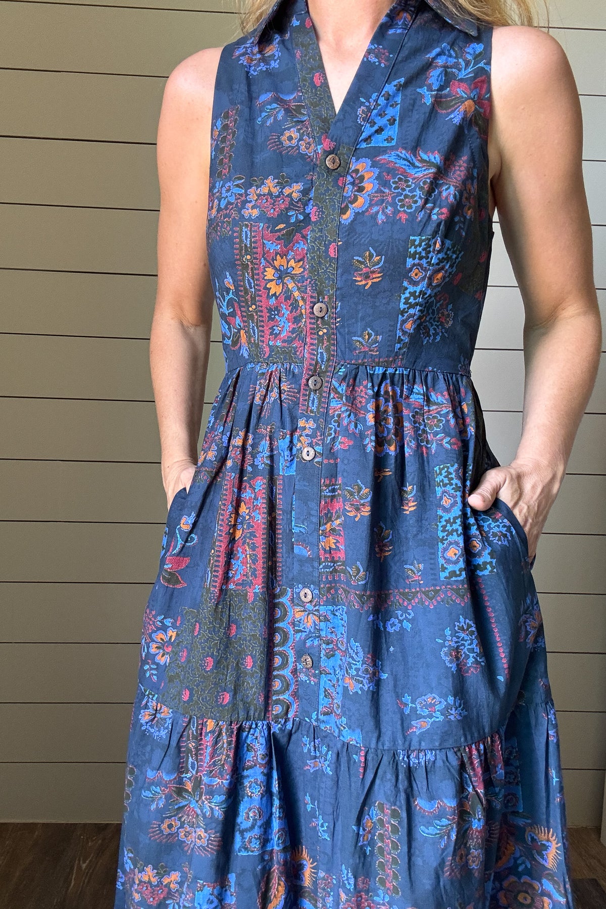 Say hello to the Indigo Garden Maxi Dress—an easy favorite for warm days. Made from 100% cotton, this sleeveless maxi is soft, breathable, and light. The button-front bodice and collared neckline give it a clean, polished shape, while the tiered skirt keeps the look relaxed. The printed fabric features a mix of floral and geometric designs in rich indigo, rust, and blue tones. It’s unlined, so it feels cool and comfortable, and yes—it has pockets. Dress it up or down, this one goes wherever your day takes y