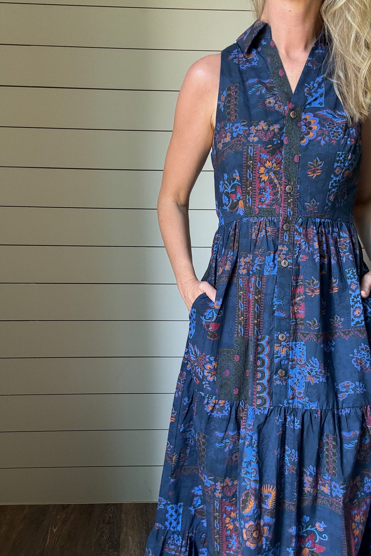 Say hello to the Indigo Garden Maxi Dress—an easy favorite for warm days. Made from 100% cotton, this sleeveless maxi is soft, breathable, and light. The button-front bodice and collared neckline give it a clean, polished shape, while the tiered skirt keeps the look relaxed. The printed fabric features a mix of floral and geometric designs in rich indigo, rust, and blue tones. It’s unlined, so it feels cool and comfortable, and yes—it has pockets. Dress it up or down, this one goes wherever your day takes y