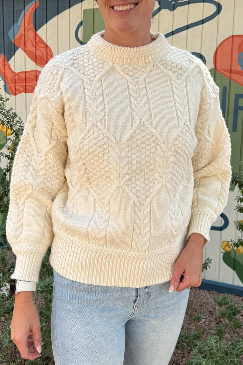 Classic cable knit gets a modern update in this ivory sweater. Designed with intricate knit detailing on the front and sleeves, it features a surprise open-back cutout that adds a chic twist to this timeless style. Soft, cozy, and versatile — it’s the perfect piece for effortless clothing and everyday wear.