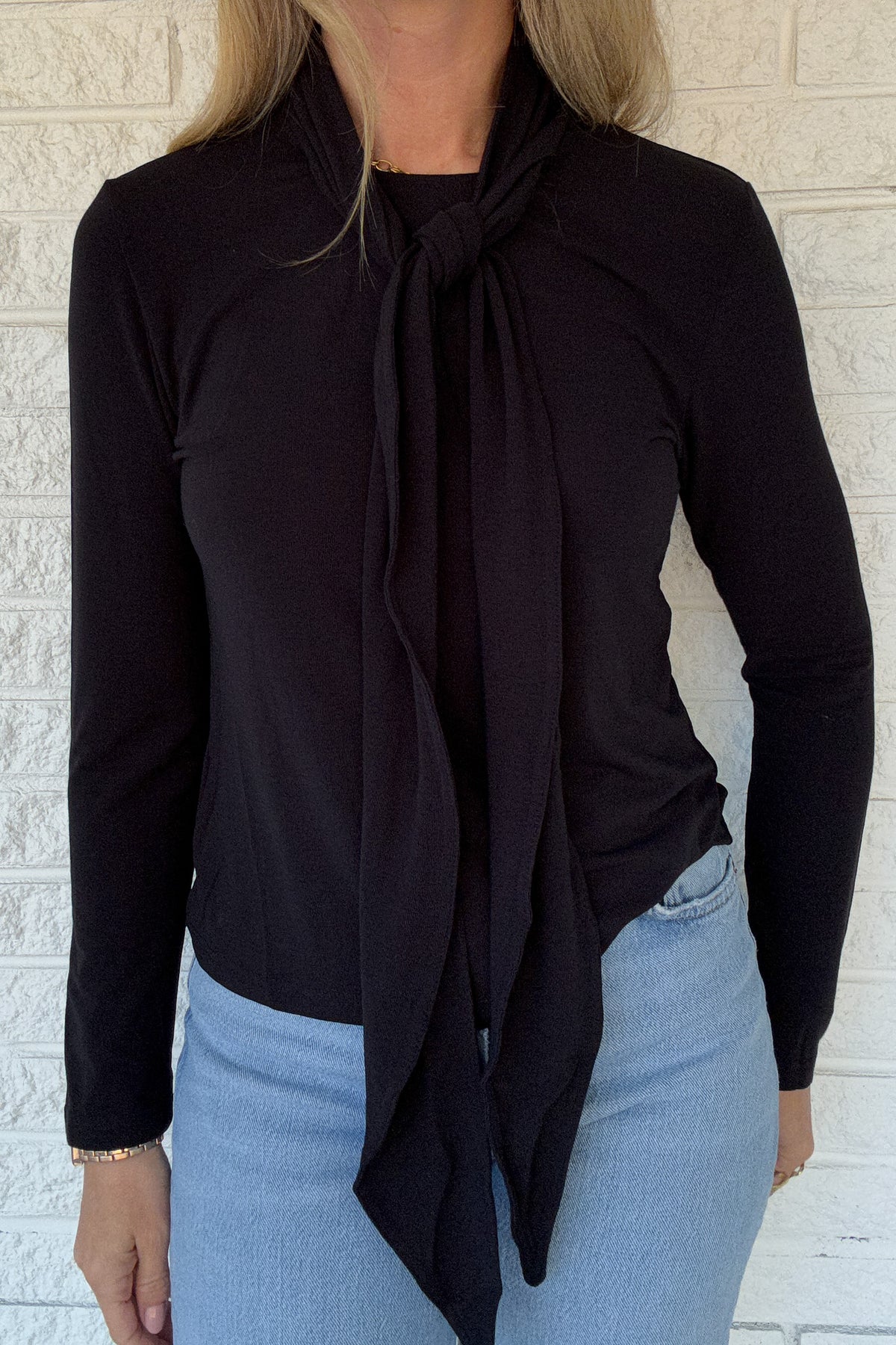 Designed in Spain, this black knit top brings an elegant touch to everyday dressing. The soft stretch fabric drapes beautifully, while the attached tie neckline adds a polished finish. Effortless yet refined, it’s the perfect piece to wear solo or layered under blazers, vests, or cardigans