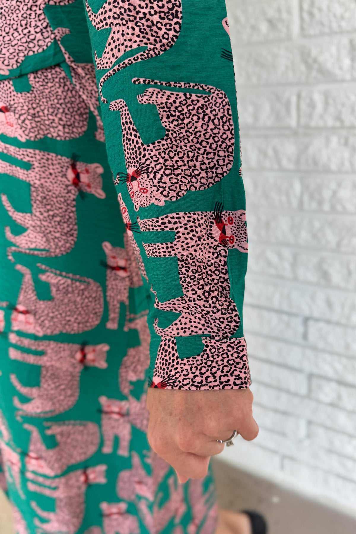 Designed in Spain, this playful shirt dress adds a touch of charm to your everyday wardrobe. Featuring a button-up front, classic collar, and an adjustable waist tie, it blends tailored structure with easy comfort. The bold green base and pink leopard print make it a fun, standout piece that’s perfect for workdays, weekends, or travel.