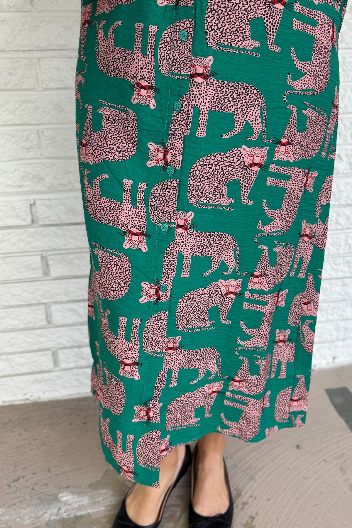 Designed in Spain, this playful shirt dress adds a touch of charm to your everyday wardrobe. Featuring a button-up front, classic collar, and an adjustable waist tie, it blends tailored structure with easy comfort. The bold green base and pink leopard print make it a fun, standout piece that’s perfect for workdays, weekends, or travel.