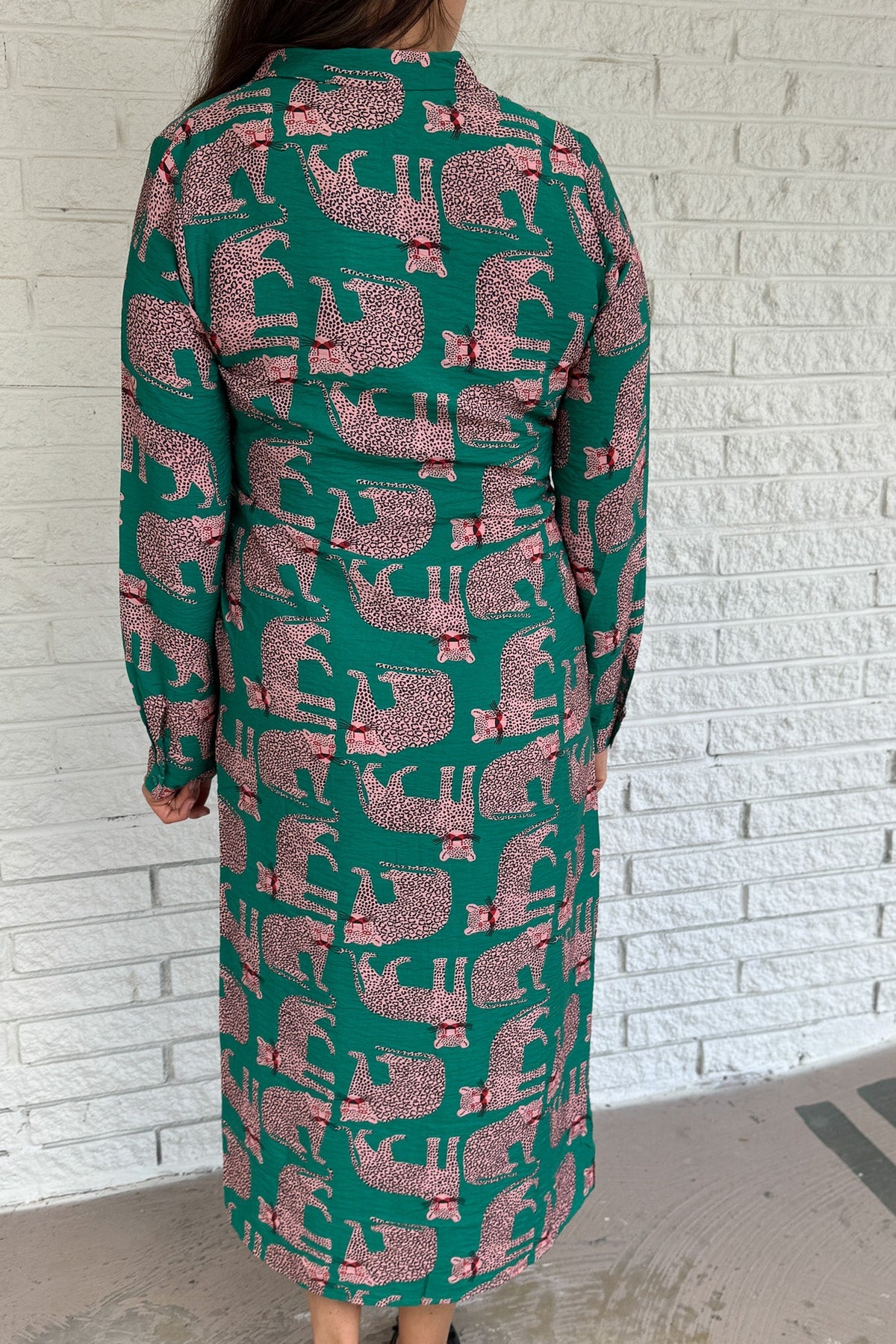 Designed in Spain, this playful shirt dress adds a touch of charm to your everyday wardrobe. Featuring a button-up front, classic collar, and an adjustable waist tie, it blends tailored structure with easy comfort. The bold green base and pink leopard print make it a fun, standout piece that’s perfect for workdays, weekends, or travel.