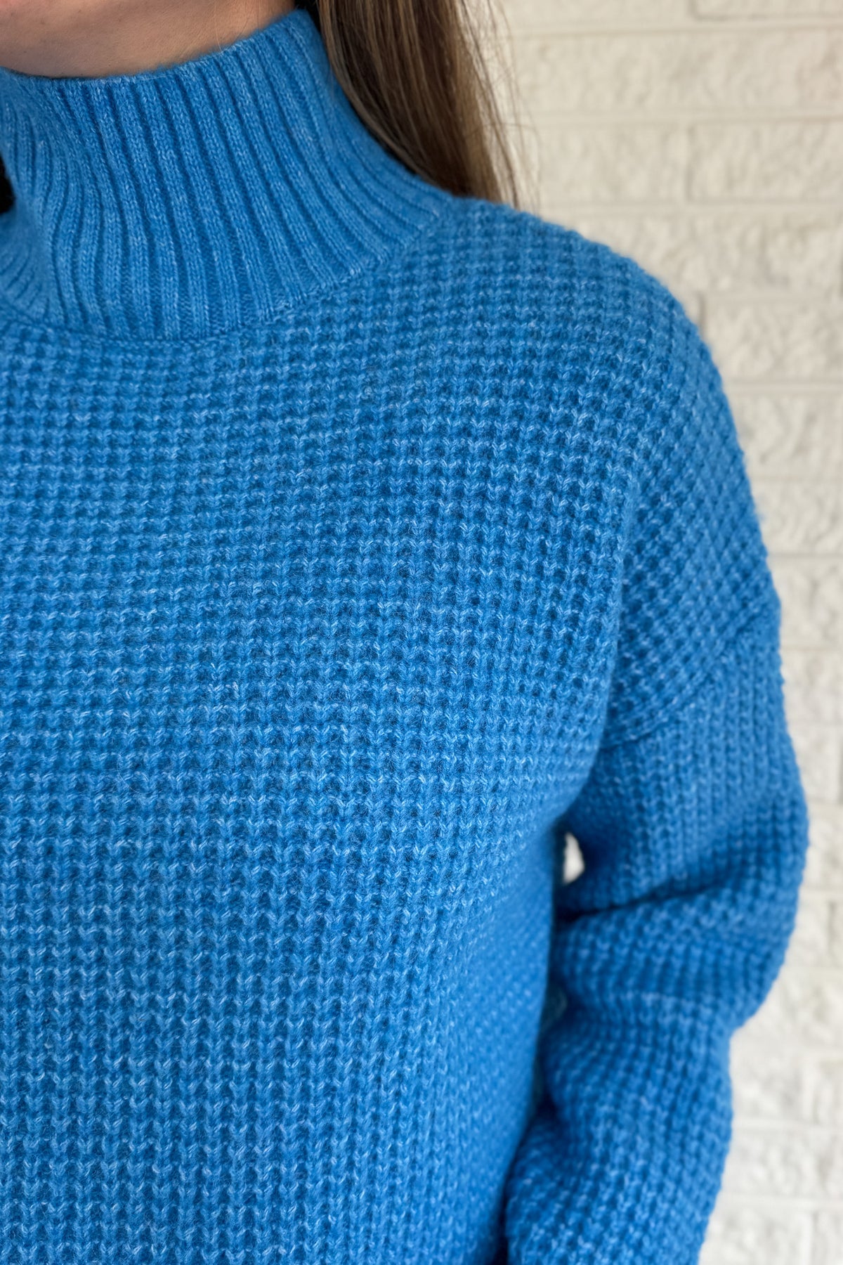 This bold blue oversized sweater brings warmth and style together in one easy piece. Knitted in a soft, textured “square” weave, it features a cozy stand-up collar and ribbed finishes that keep the look clean and structured. Perfect for pairing with denim or a skirt for effortless everyday wear.