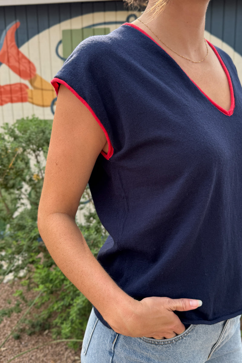Close-up of a women’s navy V-neck top featuring red contrast edging along the neckline and wide cap sleeves.